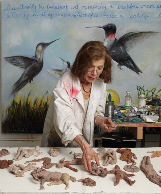 A woman in white shirt and black jacket near table with bird figurines.