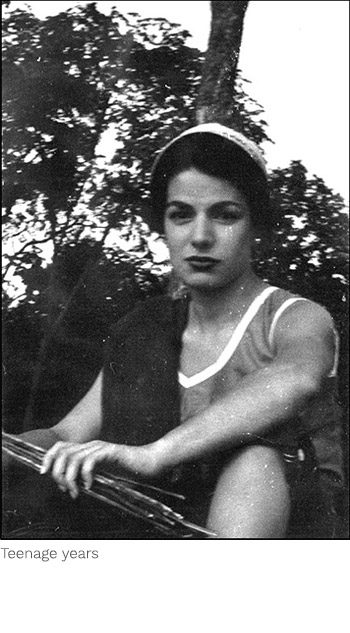 A woman sitting on the ground in front of trees.